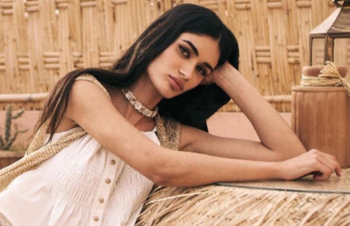 Modelo con top blanco de Maria Jose Moda, apoyada en una mesa de esparto