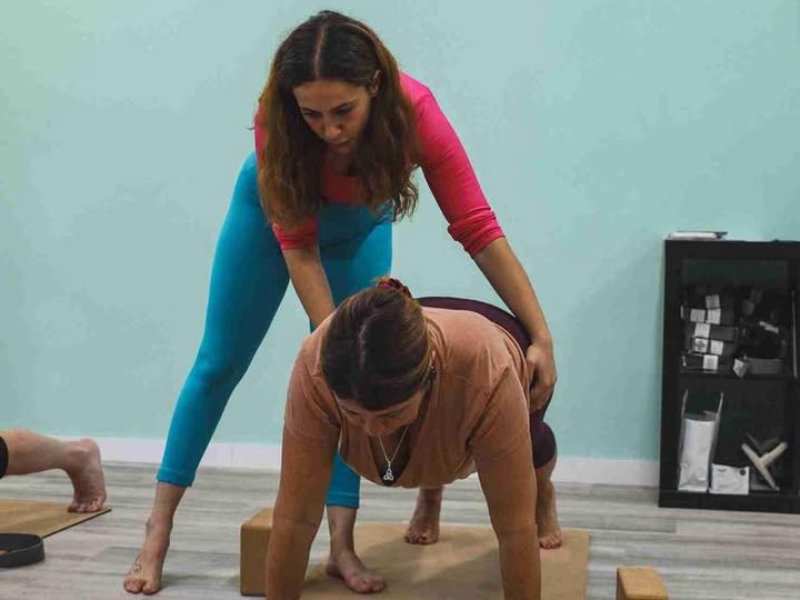 A teacher corrects the posture of a student on her mat